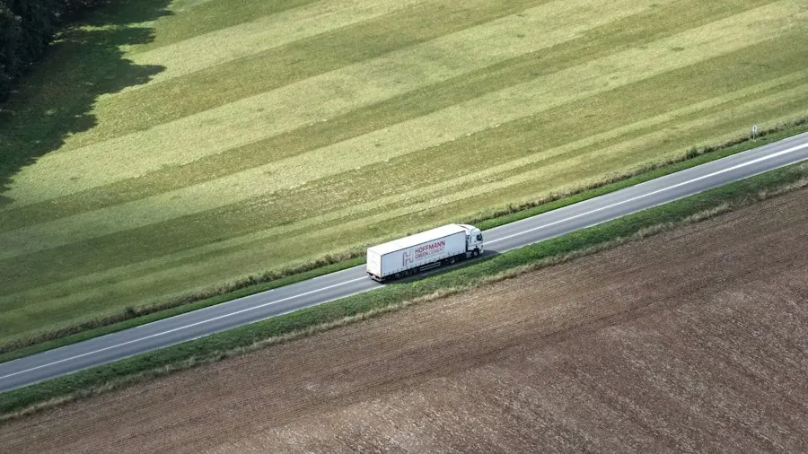 White truck traveling a road through open farm fields